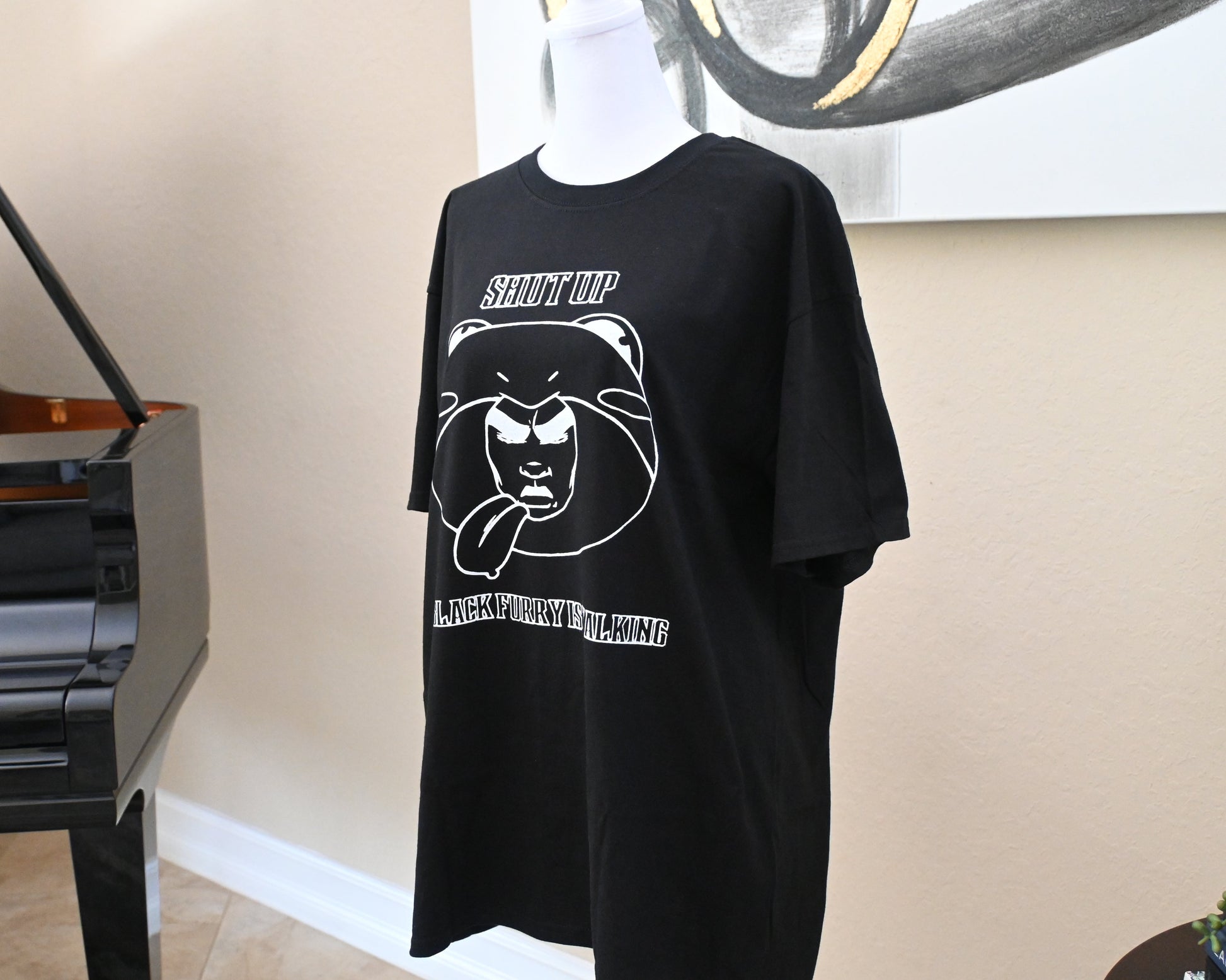 Black t-shirt with graphic design on a mannequin in front of a piano.