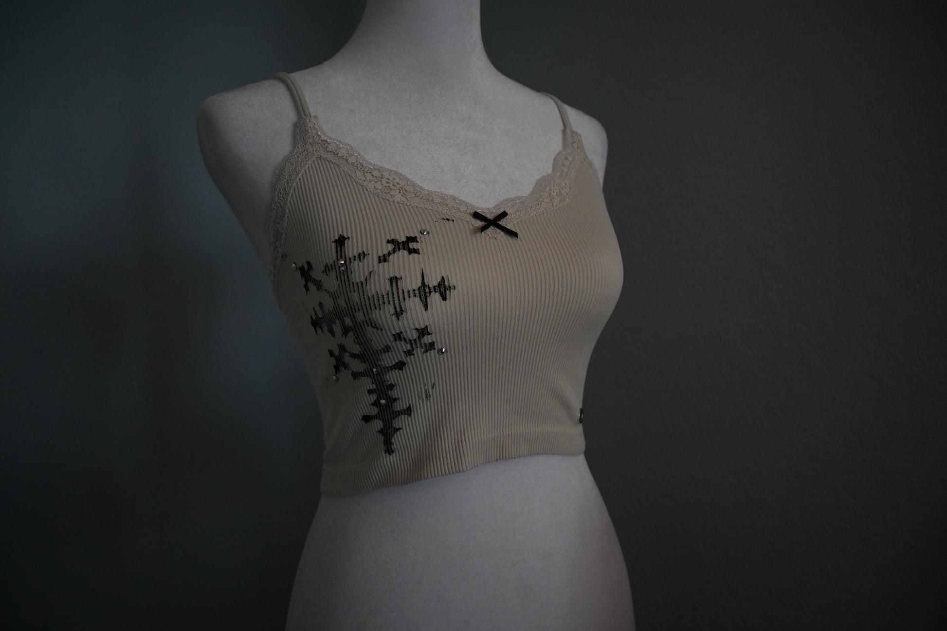 Beige tank top with black cross design on a mannequin against a dark background