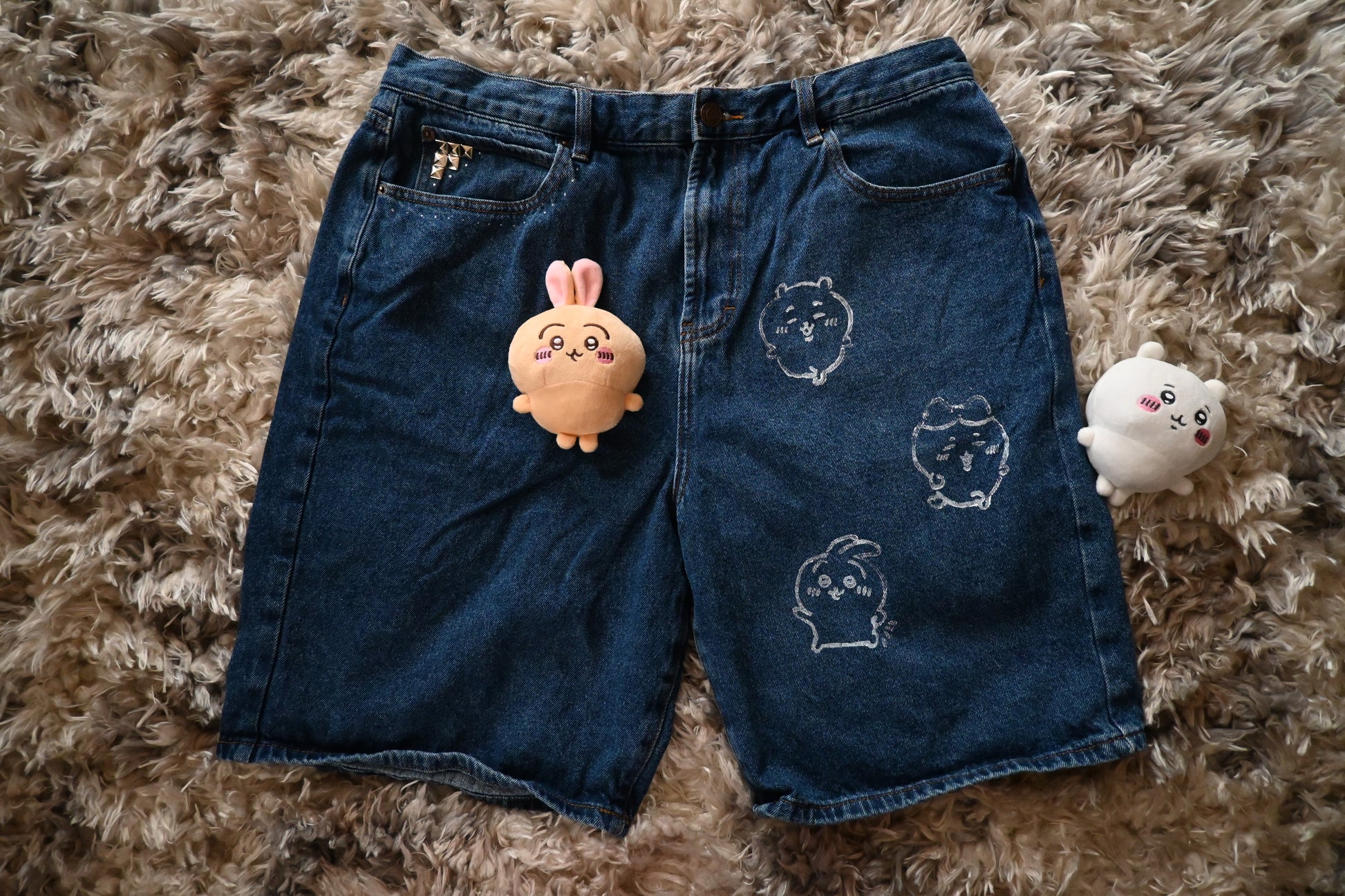 Blue denim shorts with chiikawa designs on a textured brown surface
