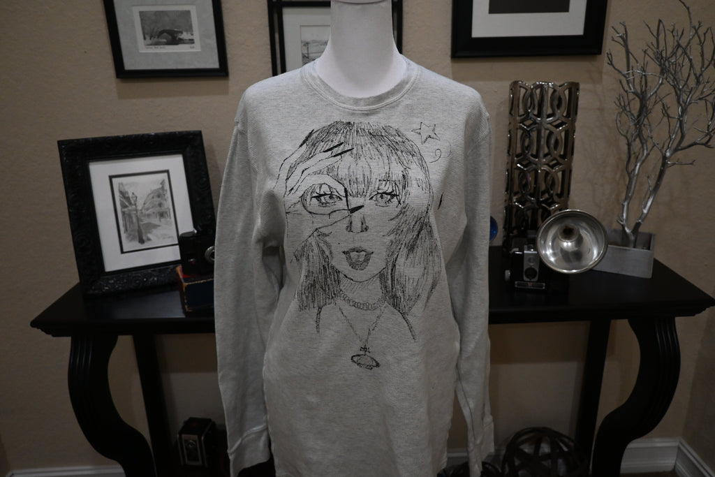 Mannequin wearing a long-sleeve shirt with a graphic design in a room with framed pictures on the wall.