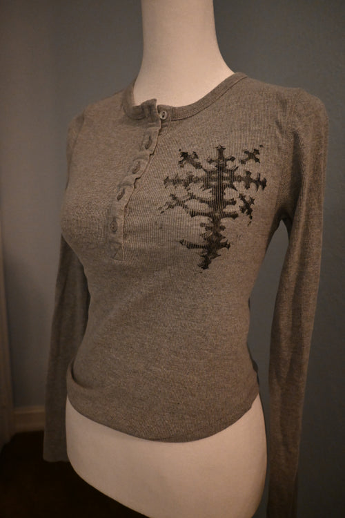 Mannequin wearing a grey sweater with a black cross on a gray background