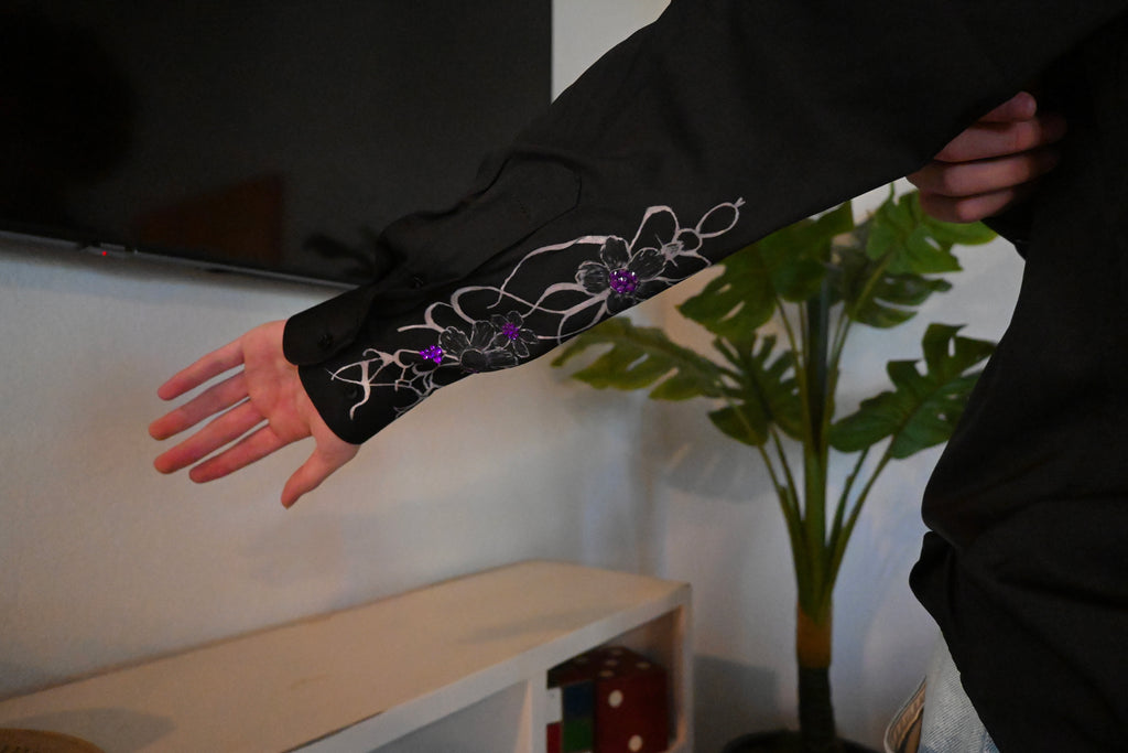 A hand painted black button up with a design on the sleeve and purple rhinestones