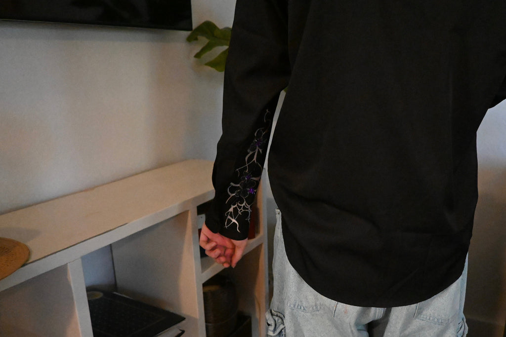 A hand painted black button up with a design on the sleeve and purple rhinestones