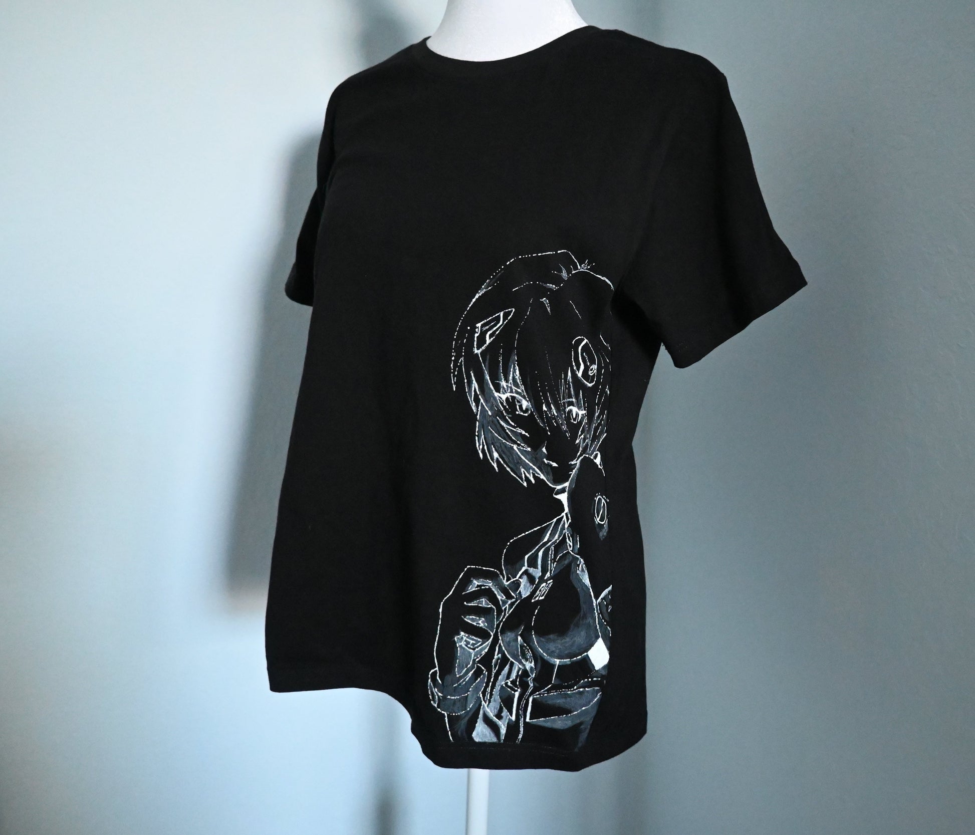 Black t-shirt with white graphic design of Rei from Evangelion on a mannequin against a light blue background