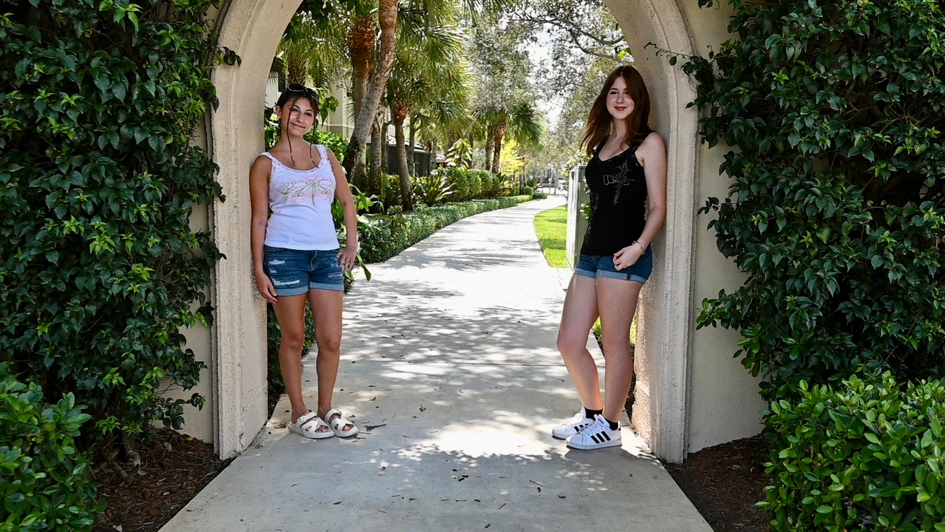 Two girls wearing hand painted lacy tank tops. One design is a green dragonfly with pink designs, and the other is a black shirt with a white cross and church.