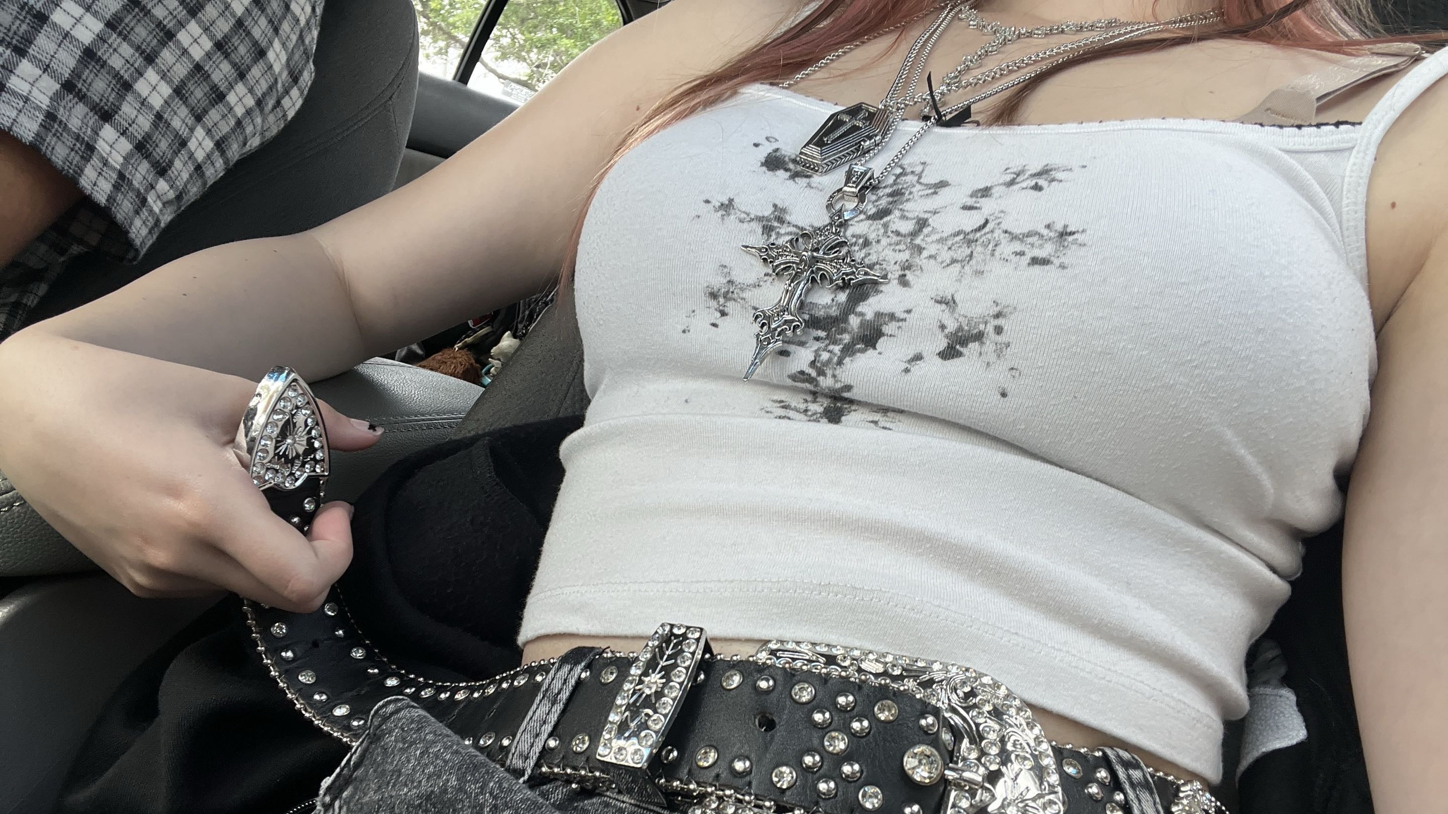 Person wearing a white tank top with a black cross design and gray jeans with a decorative belt.