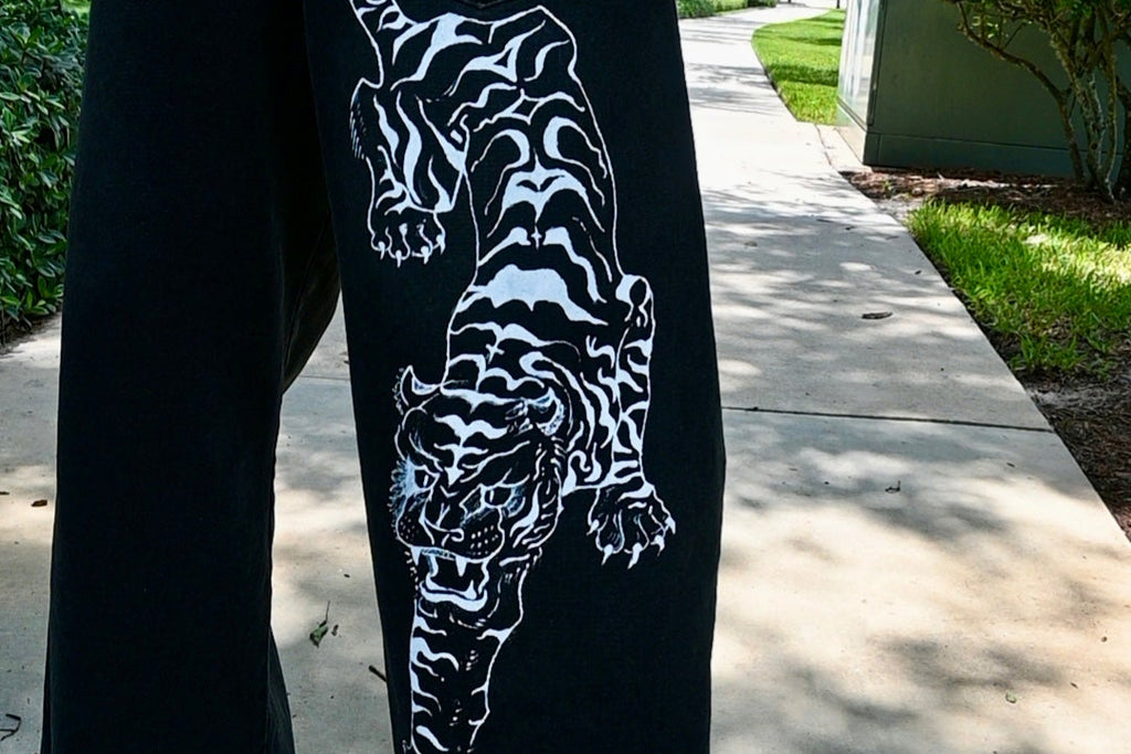 A black pair of jeans with a white tiger painted on.